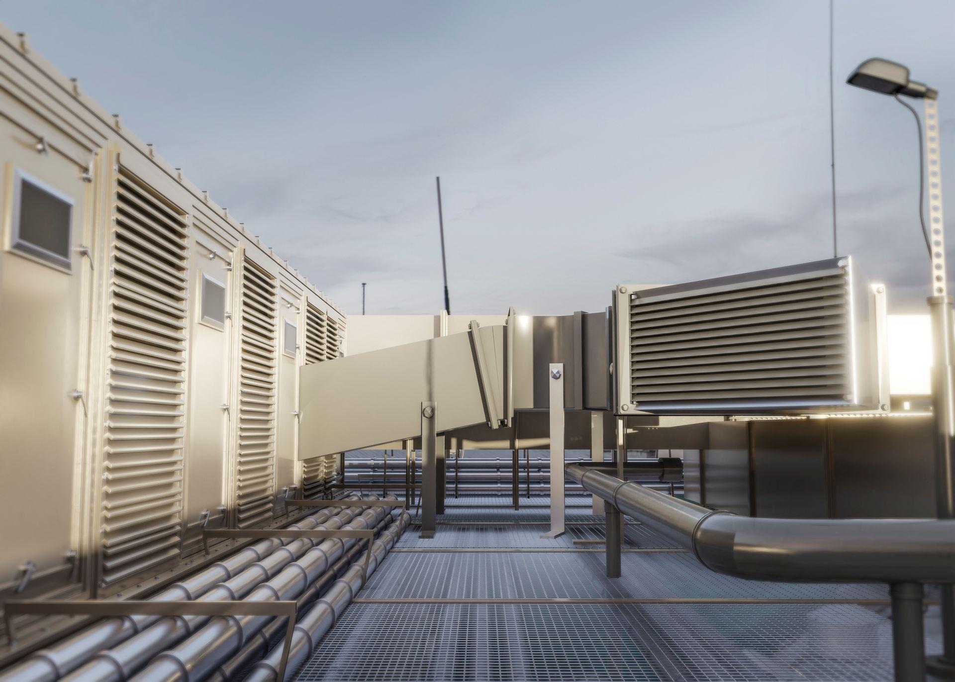 Industrial rooftop with ventilators, ducts, and metal pipes under a cloudy sky.